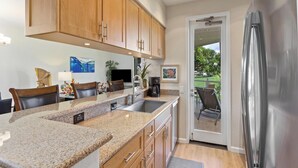 A modern kitchen with granite countertops, wooden cabinets, and a stainless steel refrigerator. - Large Floorplan - Great for Families | Grand Champions 159 (Wailea)