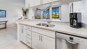A modern kitchen with white cabinets, a stainless steel sink, a Bosch dishwasher, and a coffee maker.