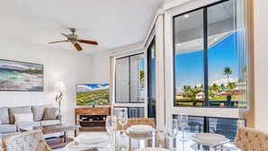 A modern dining area with a glass table, wicker chairs, and a view of a coastal landscape through large windows.