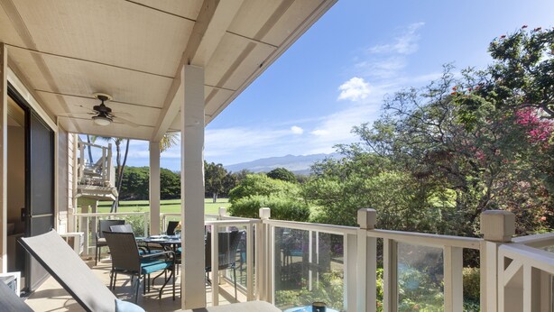 A covered outdoor area with lounge chairs and a table, overlooking a landscaped garden and distant mountains. - Platinum Rated & Golf Course Views (Wailea)