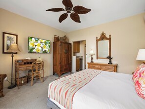 Une chambre à coucher comprenant un lit, une armoire en bois, un bureau, une chaise, un téléviseur, un ventilateur de plafond et un miroir.