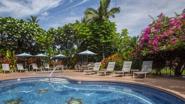 Ein Swimmingpool mit Liegestühlen und Sonnenschirmen, umgeben von üppiger Vegetation und blühenden Pflanzen.