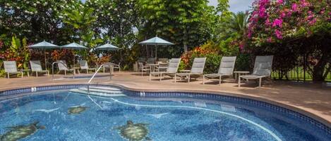 Une piscine entourée de chaises longues et de parasols, le tout baigné d’une végétation luxuriante et agrémenté de plantes en fleurs.