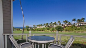 A covered patio with a round table and two wicker chairs, overlooking a golf course with palm trees and houses in the background.