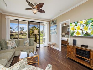 A living room with a sofa, a glass coffee table, a wooden cabinet with audio equipment, and a television on the wall.