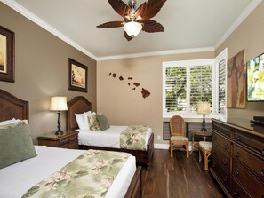 Quarto de hotel com duas camas, um ventilador de teto, uma janela com persianas, uma cômoda e uma cadeira.