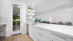 Une cuisine moderne avec des meubles blancs, un grand îlot central et une vue sur la terrasse extérieure.