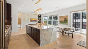 Una cocina moderna con una isla grande, suelo de madera y una zona de comedor con mesa y sillas.