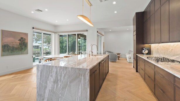 Una cocina moderna con una isla de mármol, armarios de madera oscura y un amplio ventanal con vistas al exterior.