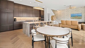 Una cocina moderna con armarios oscuros, una isla de mármol y un comedor con una mesa redonda y sillas.