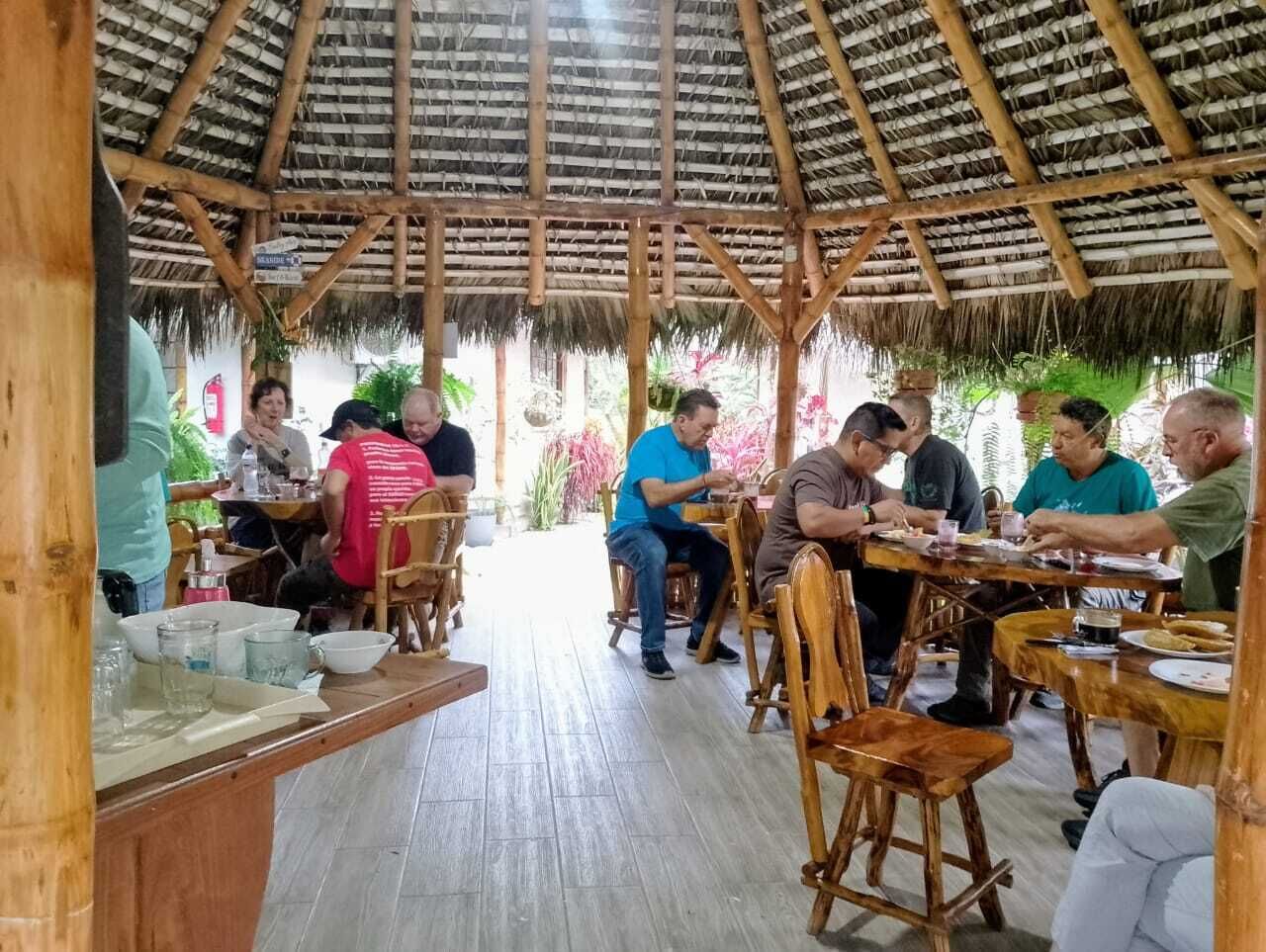 Un espacio de comedor al aire libre con techo de paja, mesas y sillas de madera.