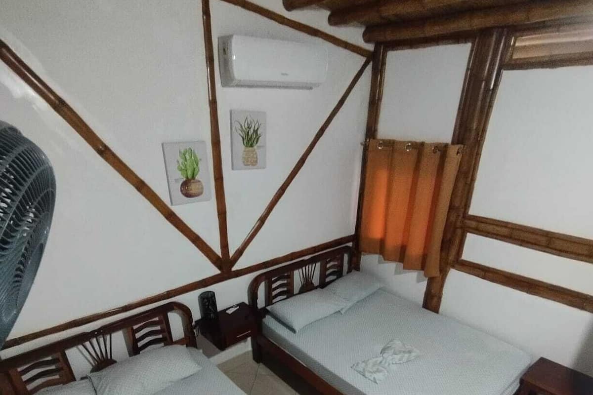 A room with two wooden beds, a wall-mounted air conditioner, and a small potted plant.