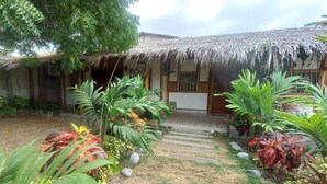 A house with a thatched roof, surrounded by a garden with various plants and a hammock. - Cabañas Riviera Pacific (Pedernales)