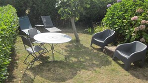 A patio with a round table and four chairs, surrounded by well-maintained hedges and flowering plants. - Pen Ty lumineux avec jardinet clos, en plein cœur de la côte de granit rose (Trégastel)