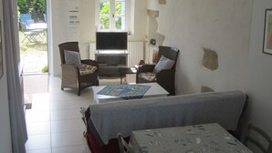 A room with a dining table, chairs, a television, and a window. - Pen Ty lumineux avec jardinet clos, en plein cœur de la côte de granit rose (Trégastel)