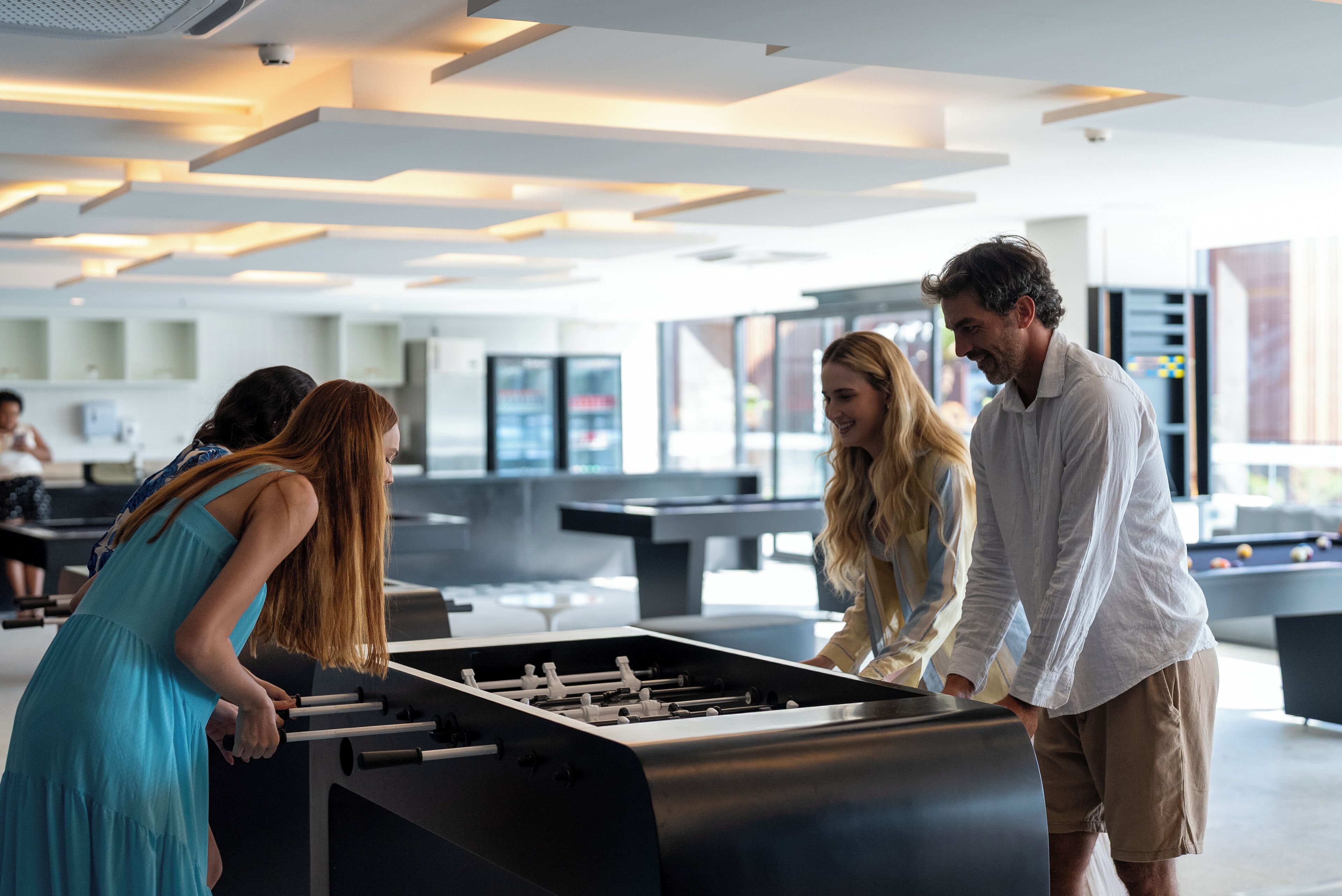 A modern indoor space with a foosball table, a pool table, and a bar area.