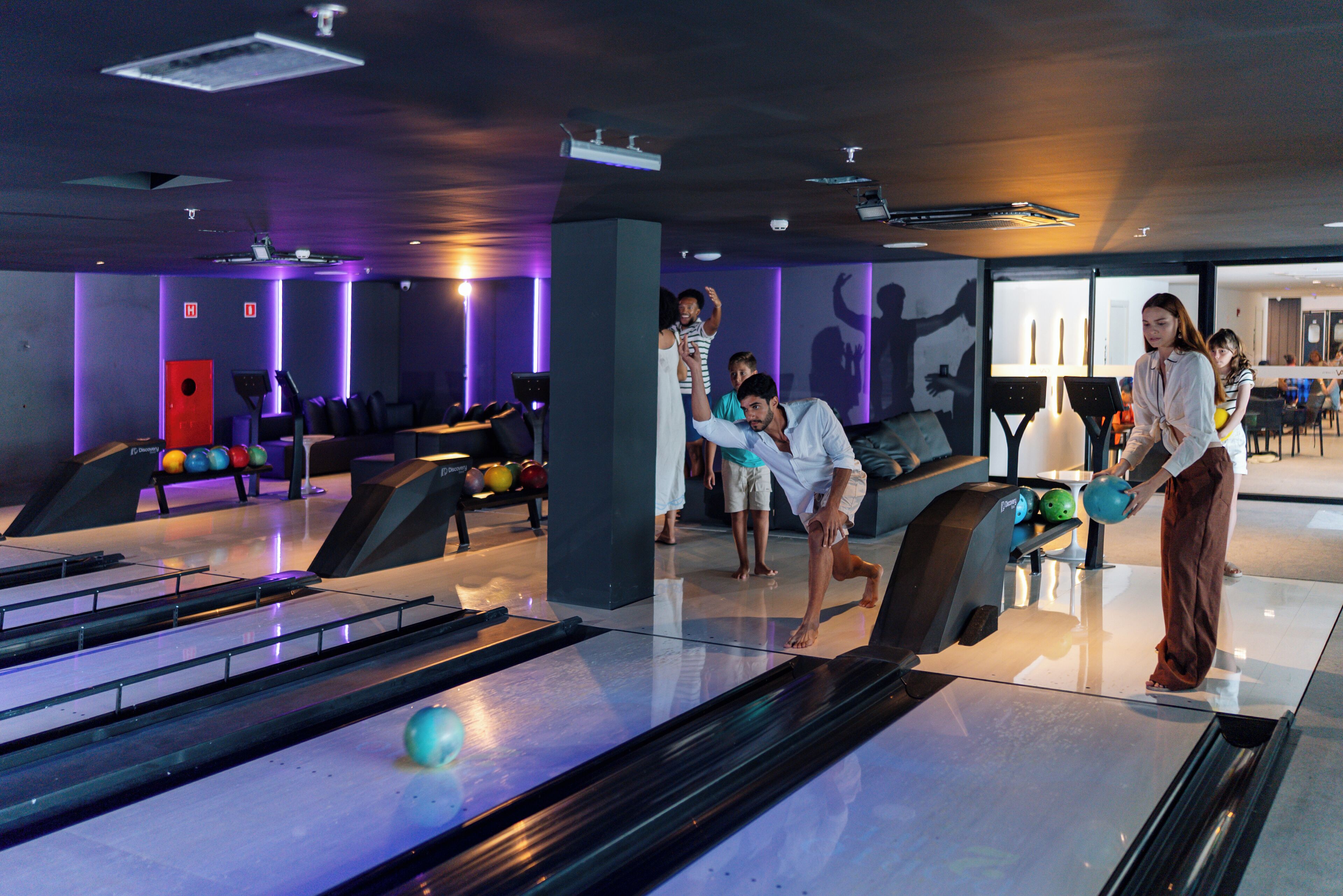 A bowling alley with multiple lanes, a red exit door, and a seating area with a couch.
