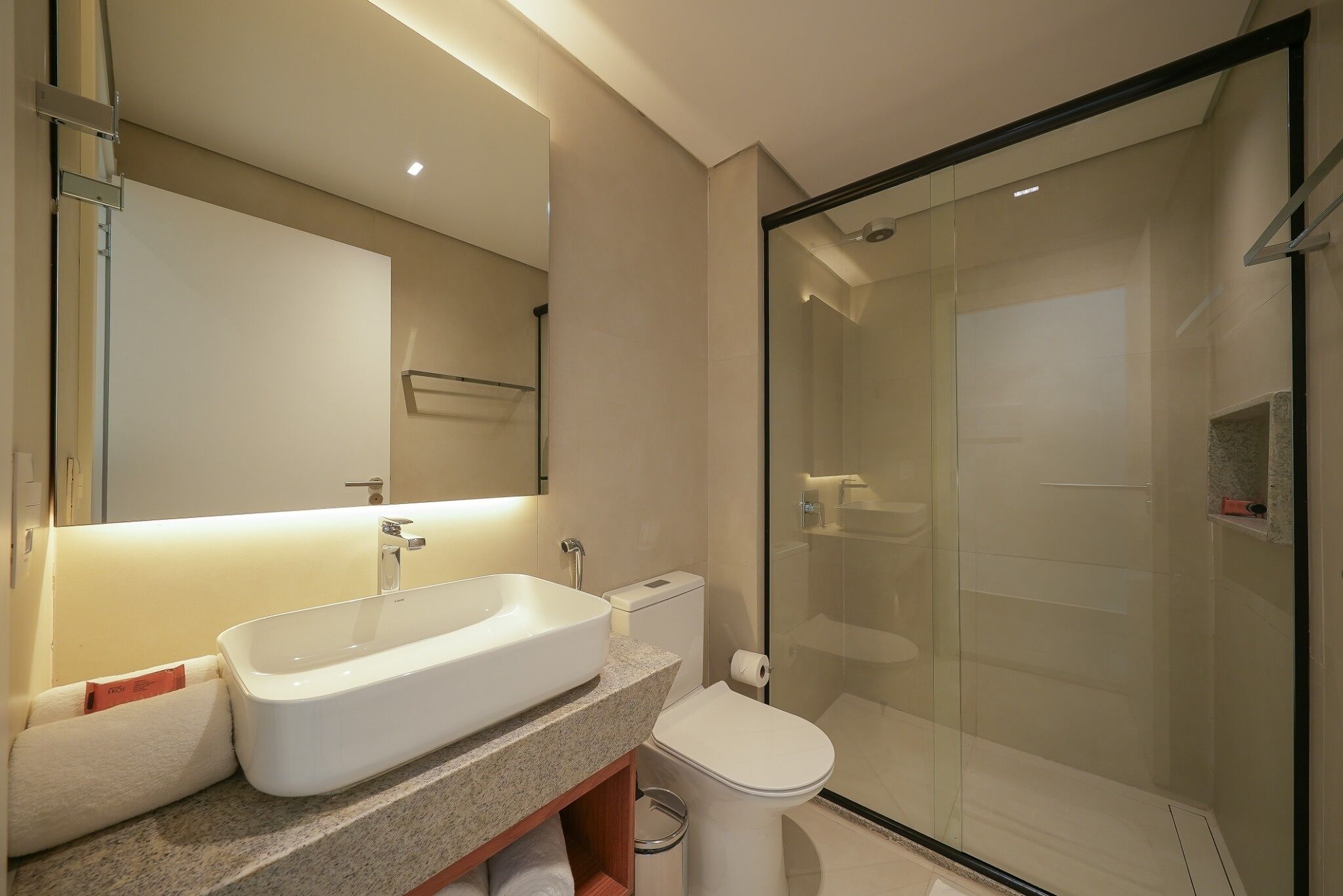 Un baño moderno con un lavamanos grande, inodoro y ducha con mampara de vidrio.