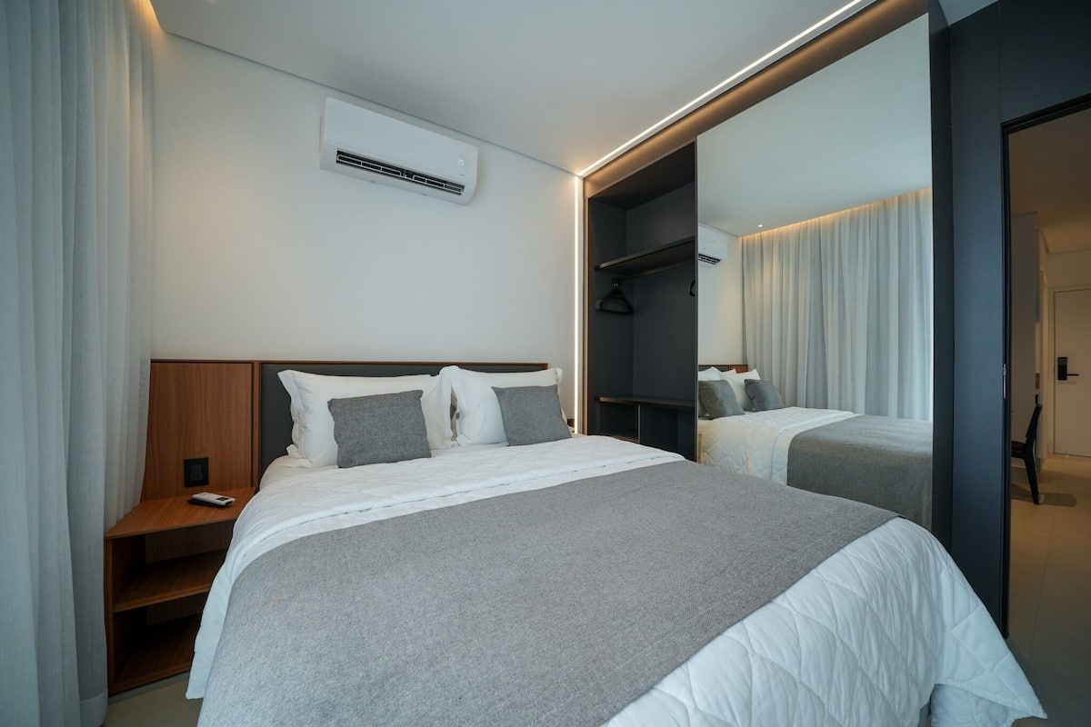 Una habitación de hotel moderna con una cama grande, una mesita de noche, un espejo y un armario.