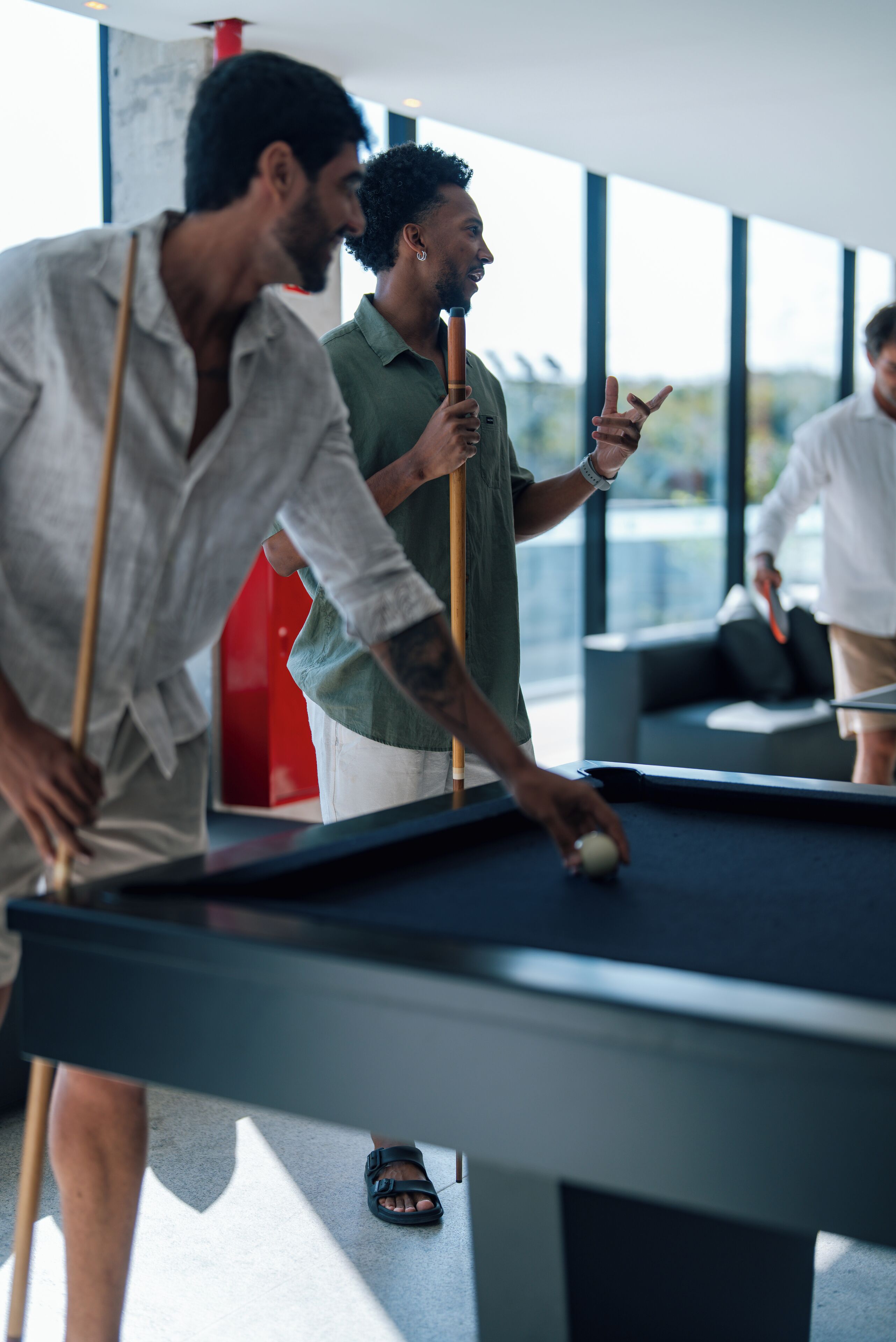 A pool table in a modern indoor setting with large windows.