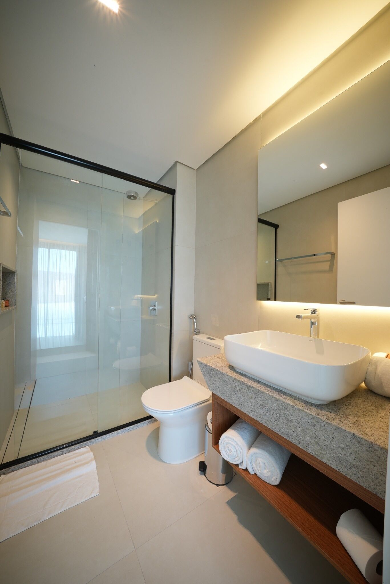 Un baño moderno con ducha envuelta en vidrio, un lavabo blanco y un espejo grande.