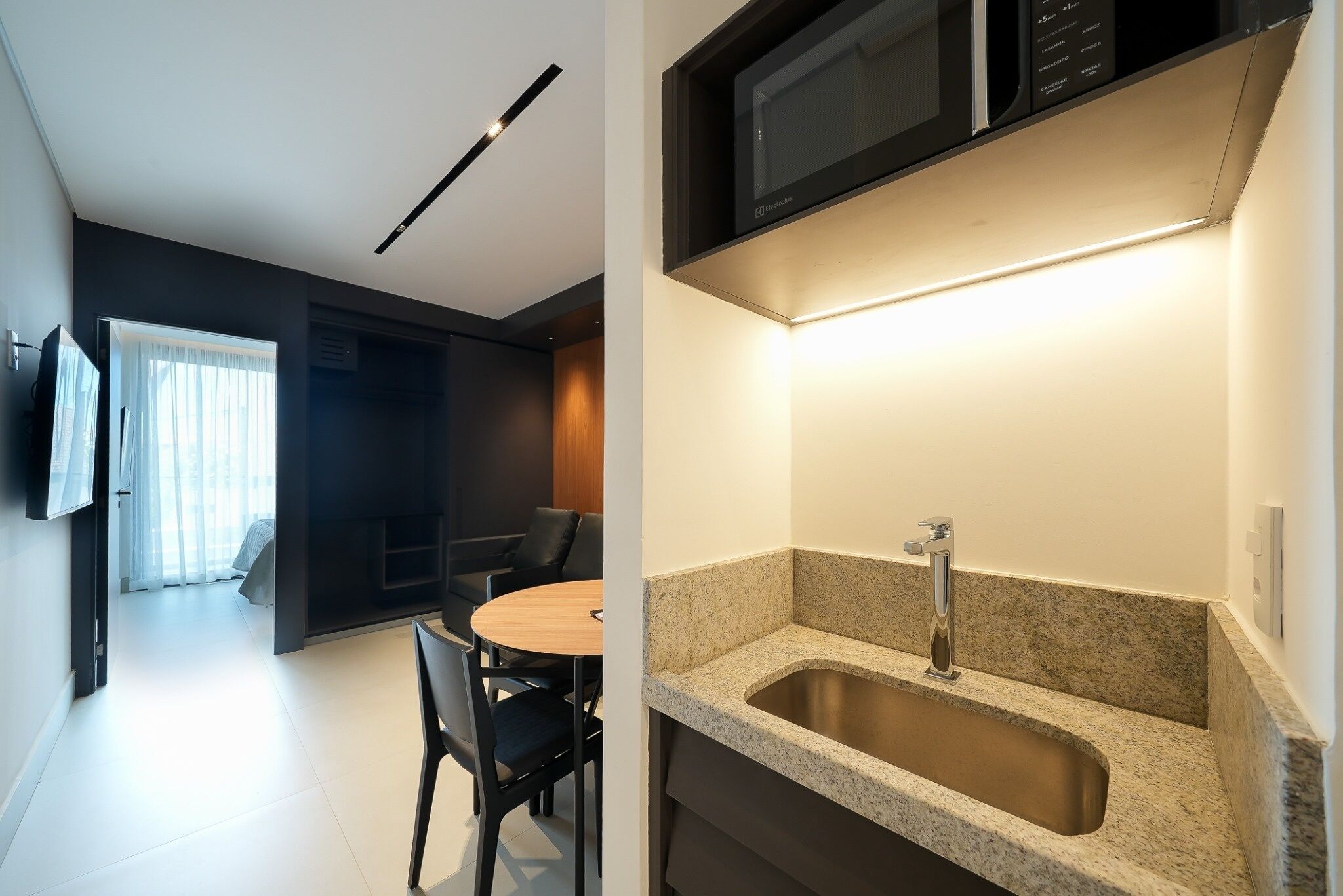 A modern kitchen with a granite countertop, stainless steel sink, and a microwave above it.