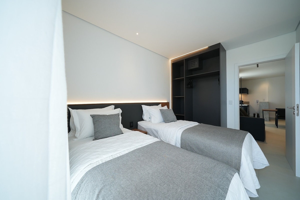 Una habitación de hotel moderna con dos camas, un vestidor y un baño visible a través de una puerta abierta.