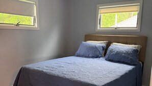 A bedroom with a bed, two windows, a ceiling fan, and a patterned rug. - Lake it Easy 2-bedroom cottage in Lyndonville (Lyndonville)