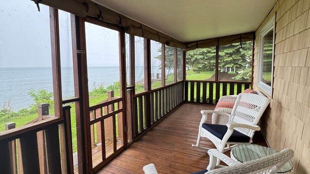 A covered porch with wooden flooring and white wicker chairs. - Lake it Easy 2-bedroom cottage in Lyndonville (Lyndonville)