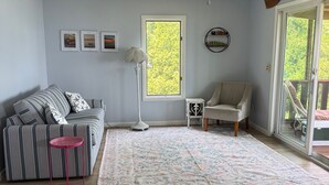A living room with a ceiling fan, a large window, a sofa, a chair, a small table, and a floor lamp. - Lake it Easy 2-bedroom cottage in Lyndonville (Lyndonville)