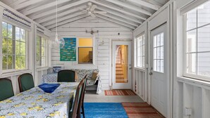 Une pièce comprenant une table à manger, des chaises, un ventilateur de plafond et une fenêtre donnant sur des arbres.