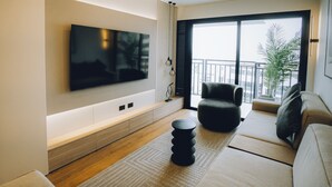 A modern living room with a flat-screen TV mounted on the wall, a sofa, a chair, and a small side table. - Luxurious brand new Apt in the heart of miraflores (Lima)