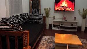 A living room with a sofa, a wooden coffee table, a TV displaying a fireplace, and a ceiling fan.