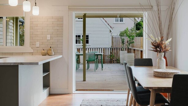 A modern kitchen with a dining area, a wooden deck, and a view of the backyard. - Stylish Retreat Near Lake, Hospital & CBD (Hamilton)