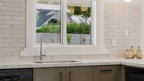 A kitchen with a window, a Bosch dishwasher, and a view of a house and greenery outside. - Stylish Retreat Near Lake, Hospital & CBD (Hamilton)