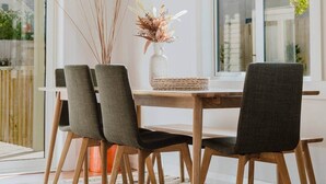 A dining area with a wooden table, four chairs, and a vase with dried plants. - Stylish Retreat Near Lake, Hospital & CBD (Hamilton)