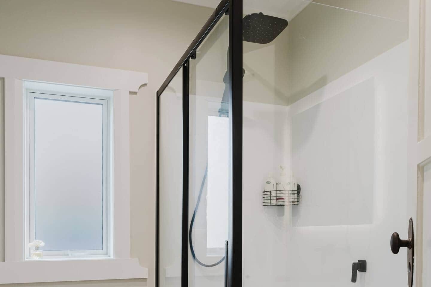 Une salle de bain moderne avec une douche à parois de verre, une porte blanche et une fenêtre.
