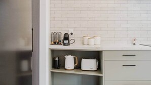 A kitchen with white brick backsplash, a coffee maker, a kettle, and a toaster on the counter. - Stylish Retreat Near Lake, Hospital & CBD (Hamilton)