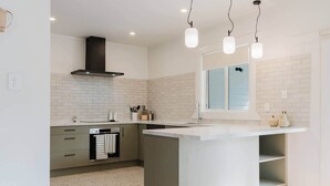A modern kitchen with a central island, white subway tiles, a stainless steel range hood, and pendant lighting. - Stylish Retreat Near Lake, Hospital & CBD (Hamilton)