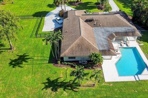 A two-story house with a swimming pool, surrounded by well-maintained lawns and palm trees.