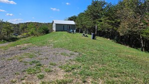 Une maison avec un toit en métal, une cour couverte d’herbe et des arbres en arrière-plan.