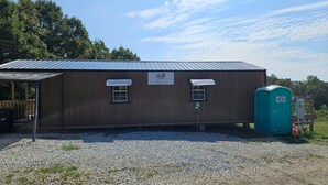 A small, single-story building with a metal roof, a wooden deck, and a portable toilet. - Hocking Hills Store Campsite #2 (Tent Site) (Washington Township)