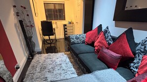 Uma sala de estar moderna com um sofá cinzento, almofadas vermelhas e pretas, um tapete felpudo branco e uma pequena mesa lateral.