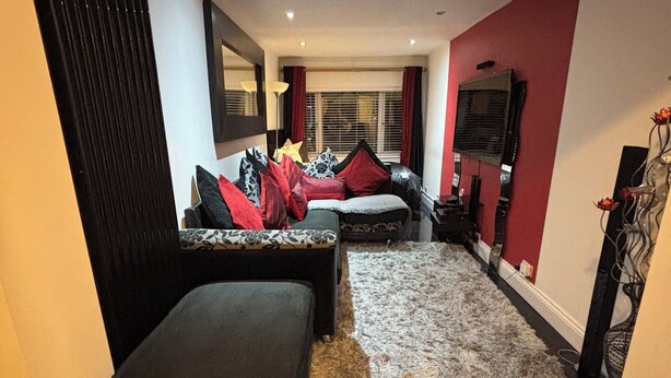 Uma sala de estar moderna com um sofá preto, um banquinho pequeno e um tapete estampado.