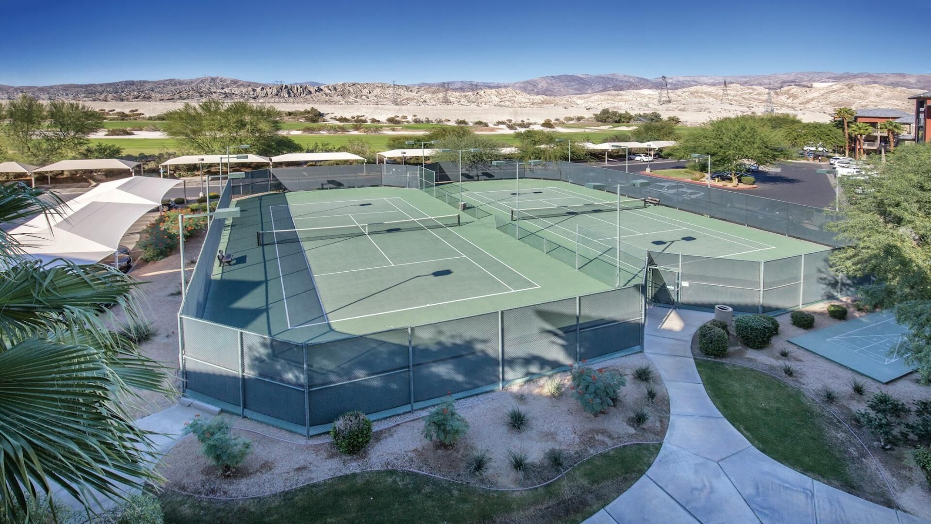 Un complexe de courts de tennis comprenant plusieurs terrains, entouré de verdure et doté d’un parking, le tout situé dans un paysage désertique.