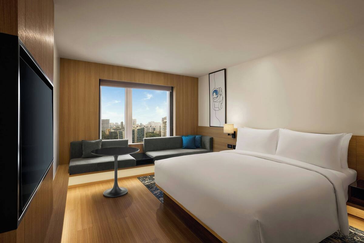 Habitació d'hotel moderna amb un llit gran, un sofà, una taula petita i una televisió.