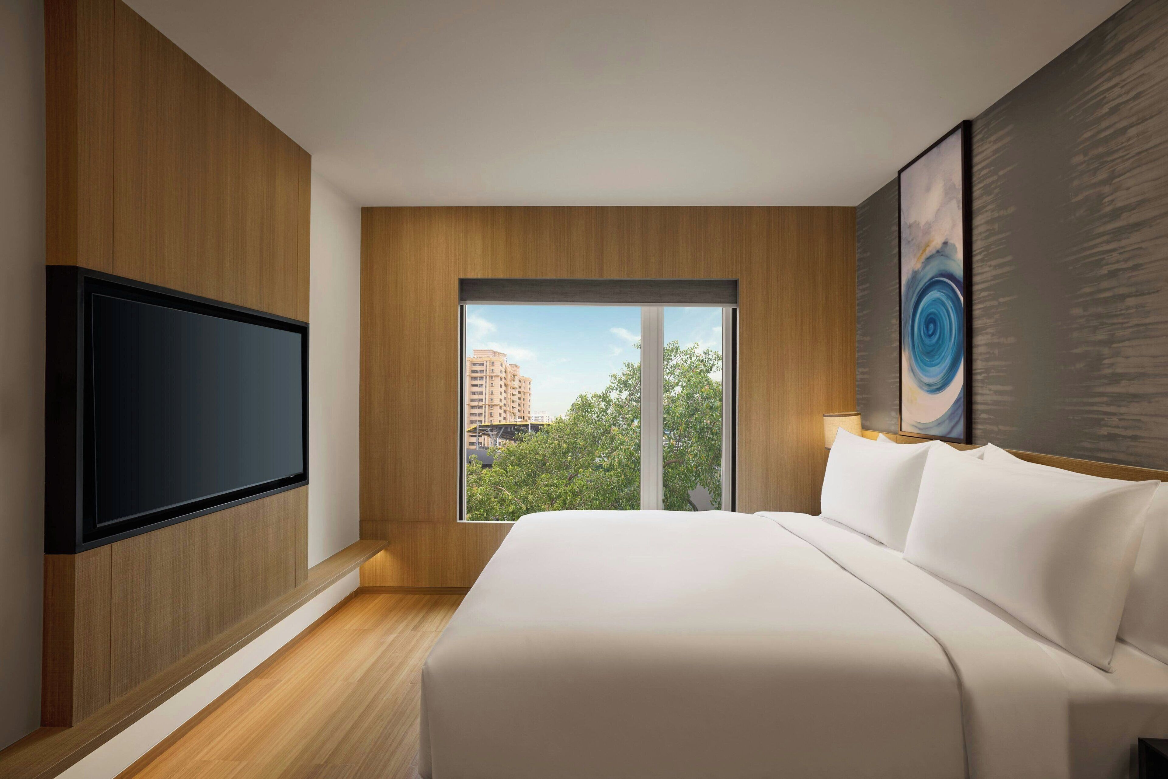 Una habitación de hotel moderna con una cama grande, un televisor de pantalla plana montado en la pared y un ventanal con vistas a la ciudad.