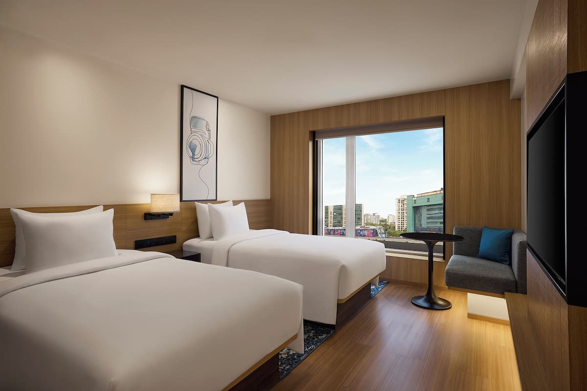 Habitació d'hotel amb dos llits, un sofà, una televisió i una finestra gran amb vista a la ciutat.