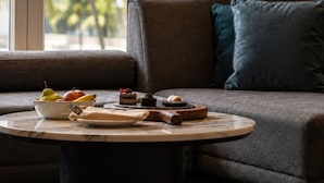 A modern living room with a sofa, a round coffee table with food items, and a view of palm trees through large windows.