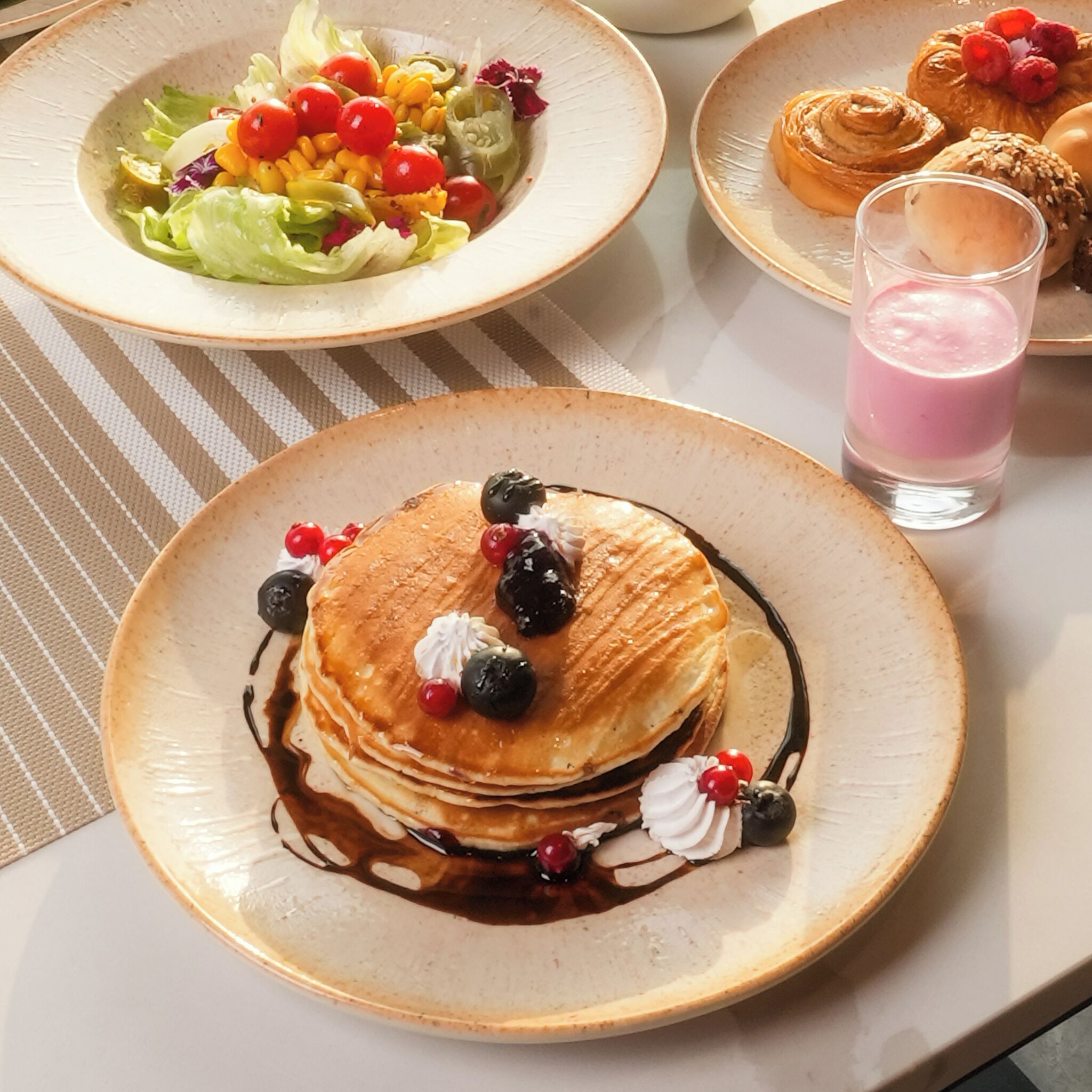 Een ontbijtsetting met pannenkoeken, bessen en een glas roze drank op een tafel.